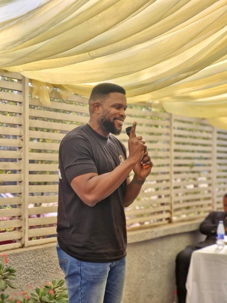 Victor speaking with a microphone at an outdoor community session under a canopy